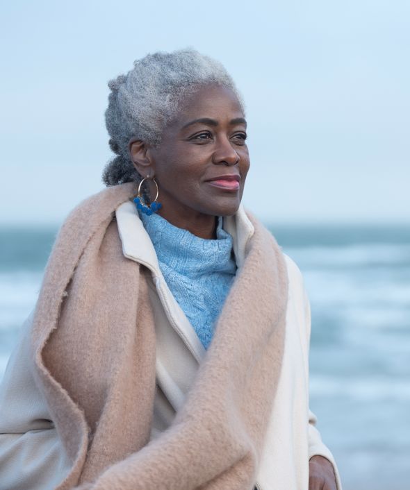 A woman over 50 smiling with the sea behind her