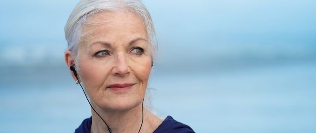 A woman over 50 with headphones in and the sea behind her
